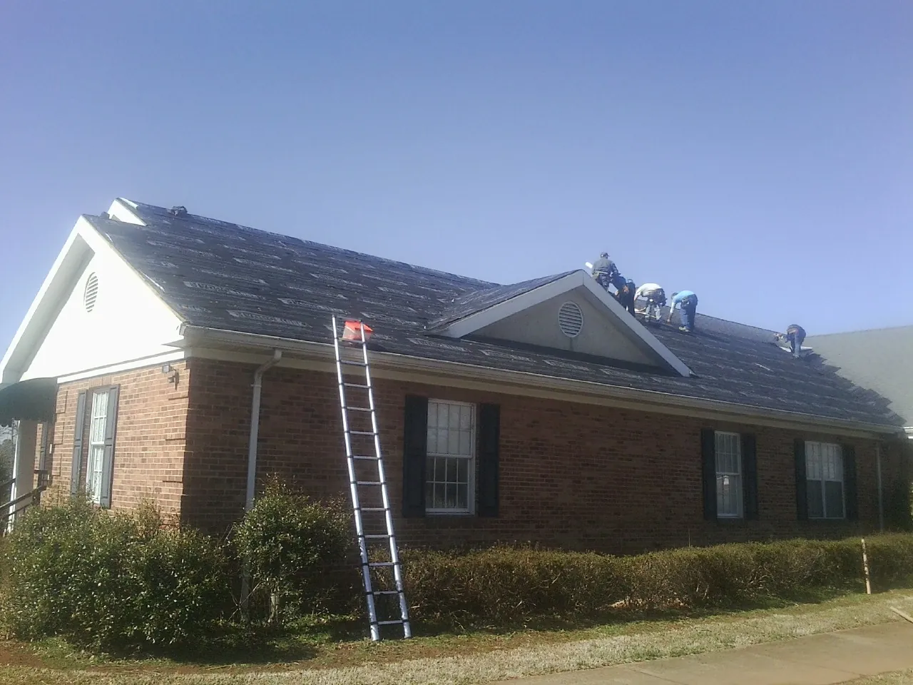 Crew tearing shingles off a brick ranch roof with a ladder set — Metal Roof Repair work by our crew in Pocahontas