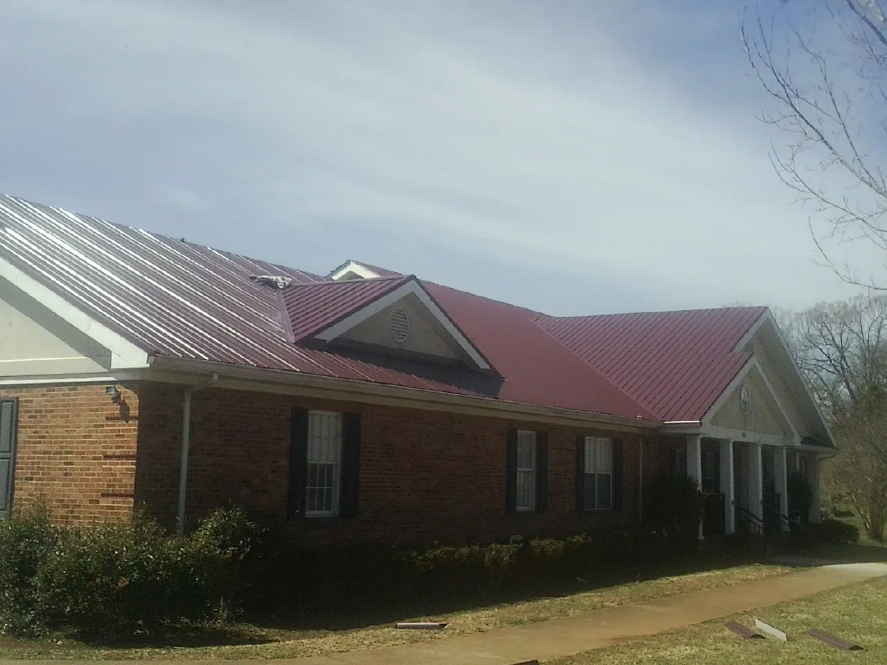 Red metal roof with gabled entries on a long brick building, from a Hail Damage Roof Repair job in Pocahontas