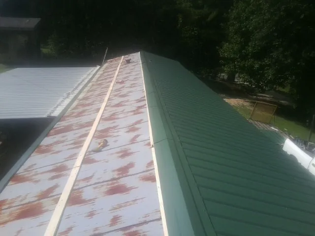 Old rusted panels beside newly installed green metal roofing — Wind Damage Roof Repair by Roofing Brothers in Pocahontas