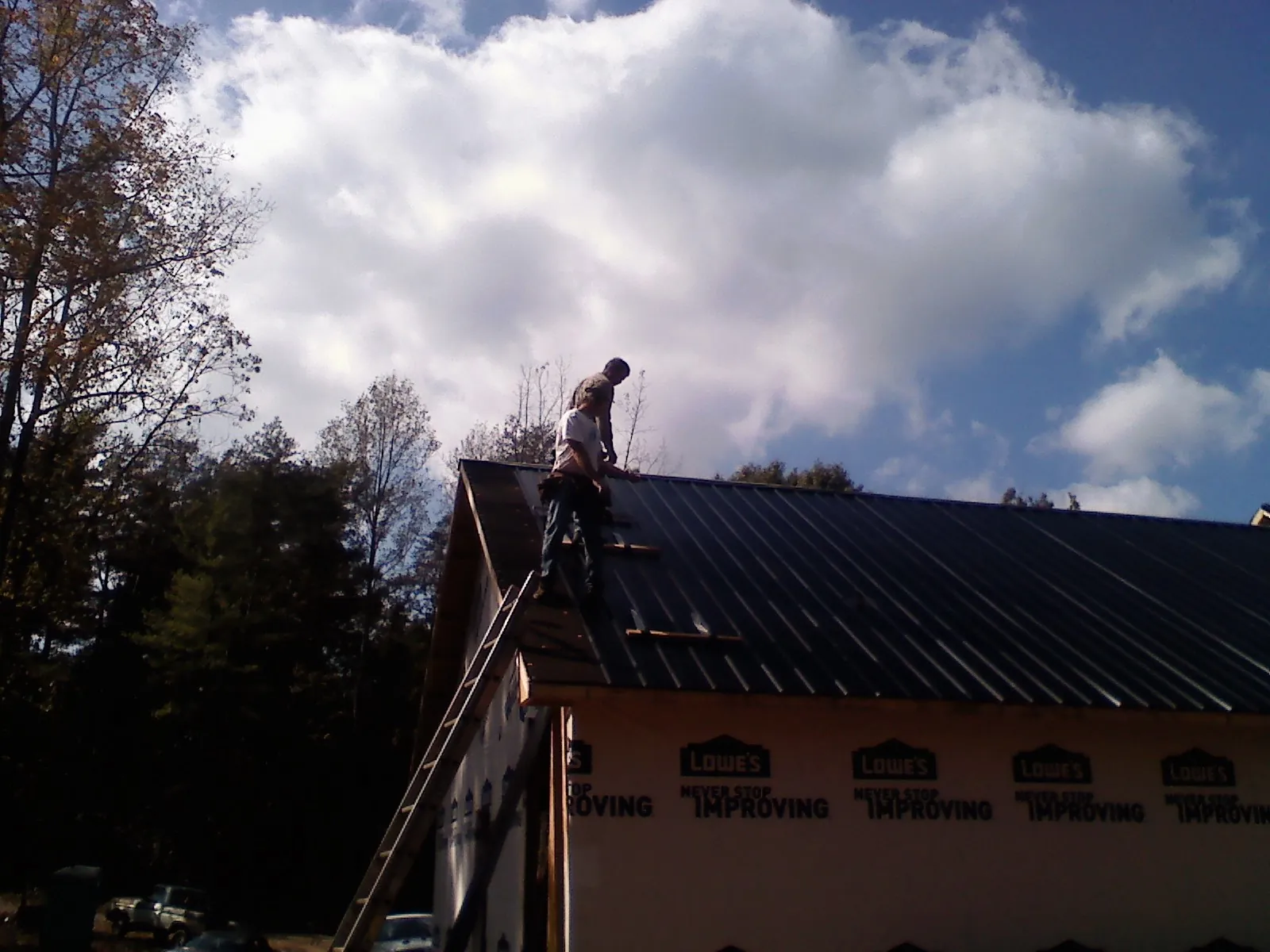 Roofer fastening dark metal panels high against a cloudy sky, from a Roof Inspection job in Pocahontas