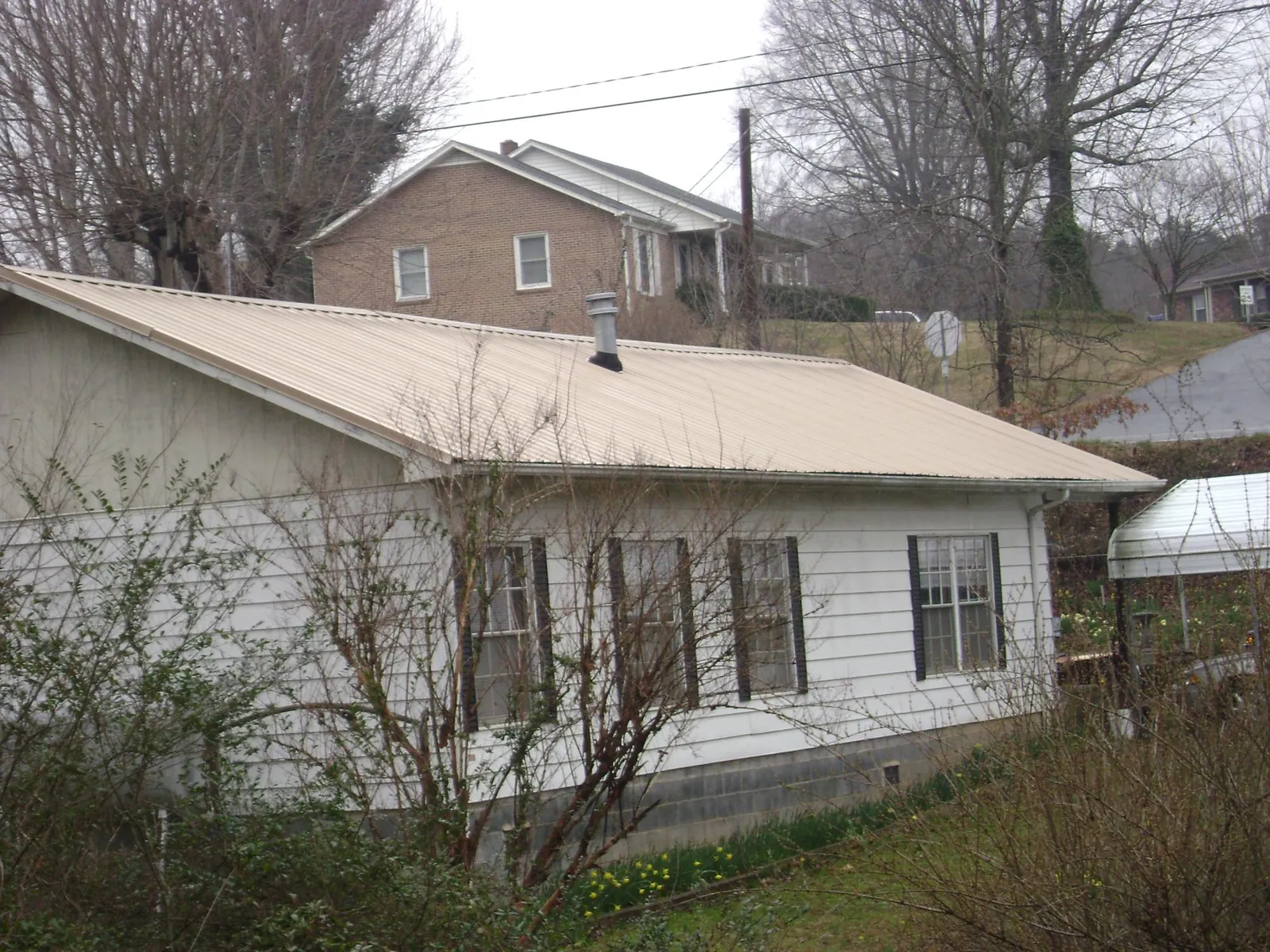 Tan metal roof on a white sided house set into a hillside — Commercial Roofing by Roofing Brothers in Pocahontas
