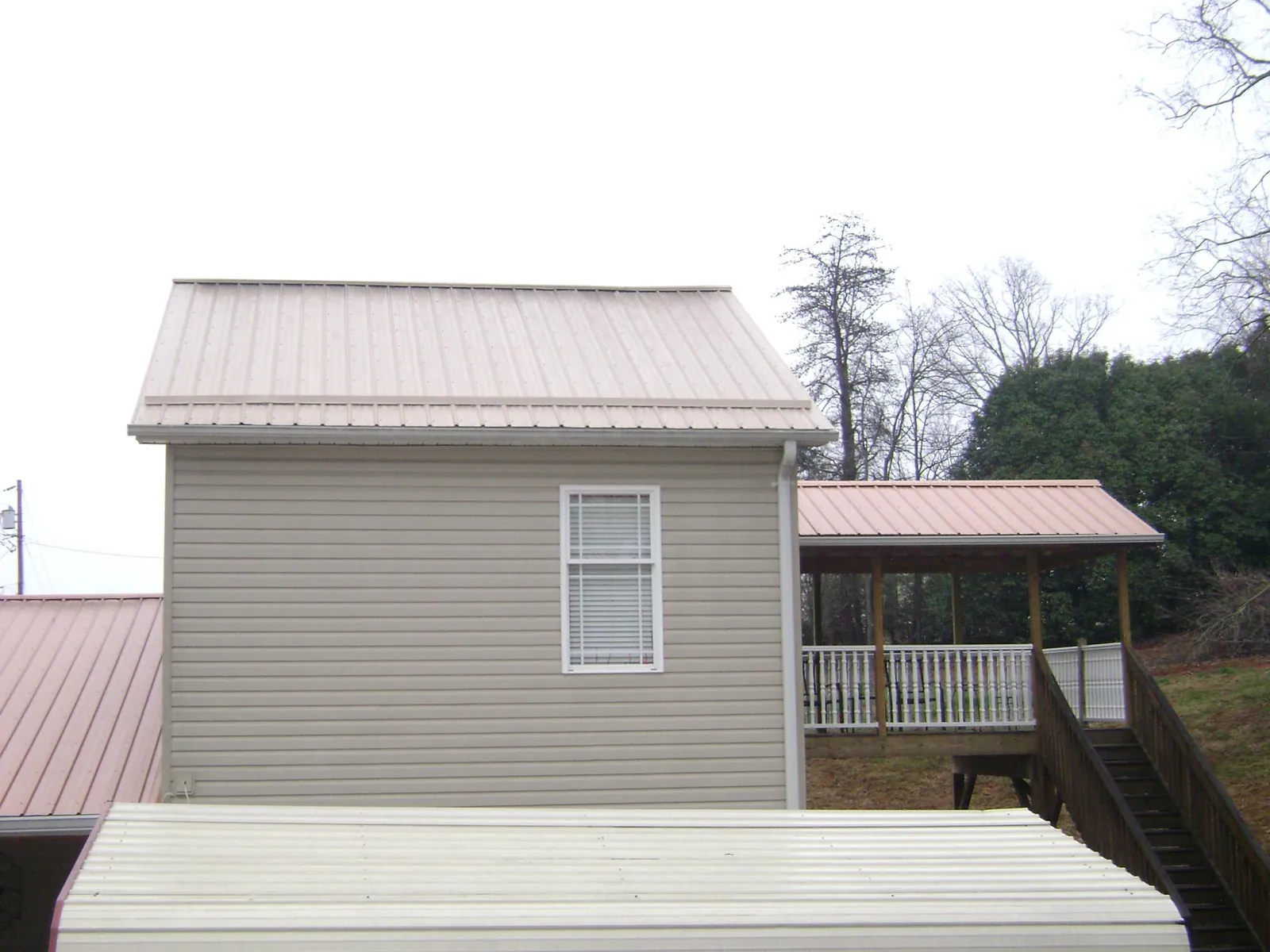 Tan metal roofs on a two story addition and attached porch, from a Roof Replacement job in Pocahontas